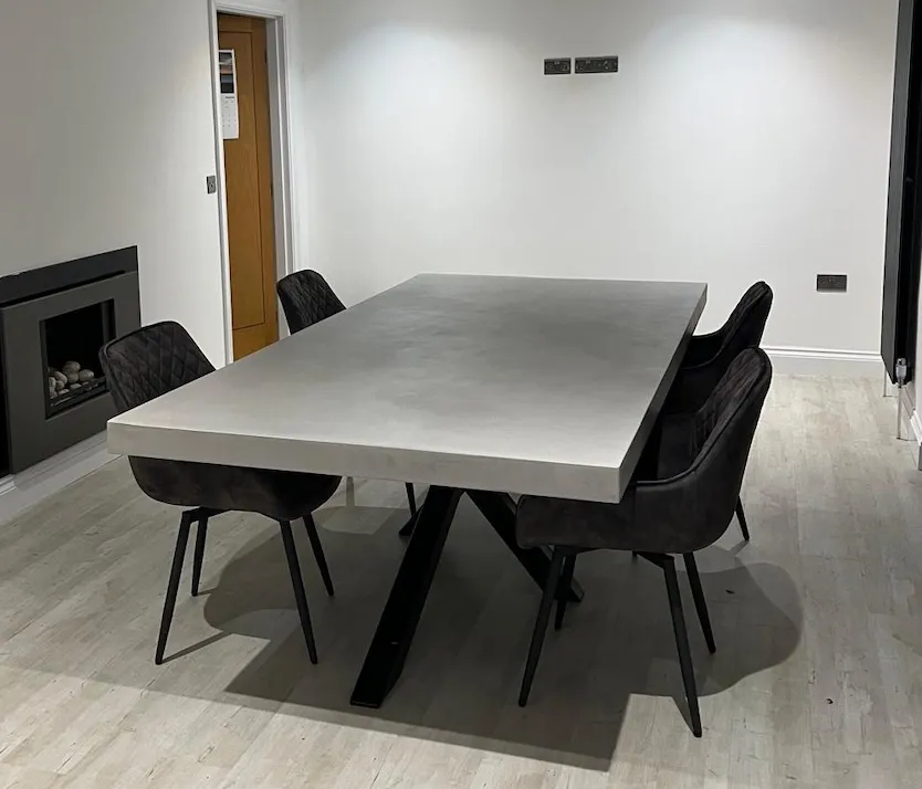 Modern dining table with a rectangular concrete top and black chairs in a minimalistic room with light wood flooring.