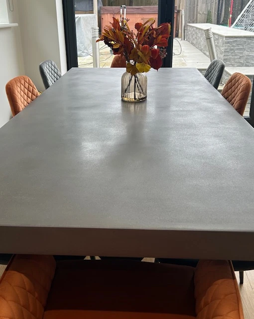 Polished concrete rectangular dining table with a glass vase of autumn leaves centerpiece, surrounded by a mix of orange and gray quilted chairs.