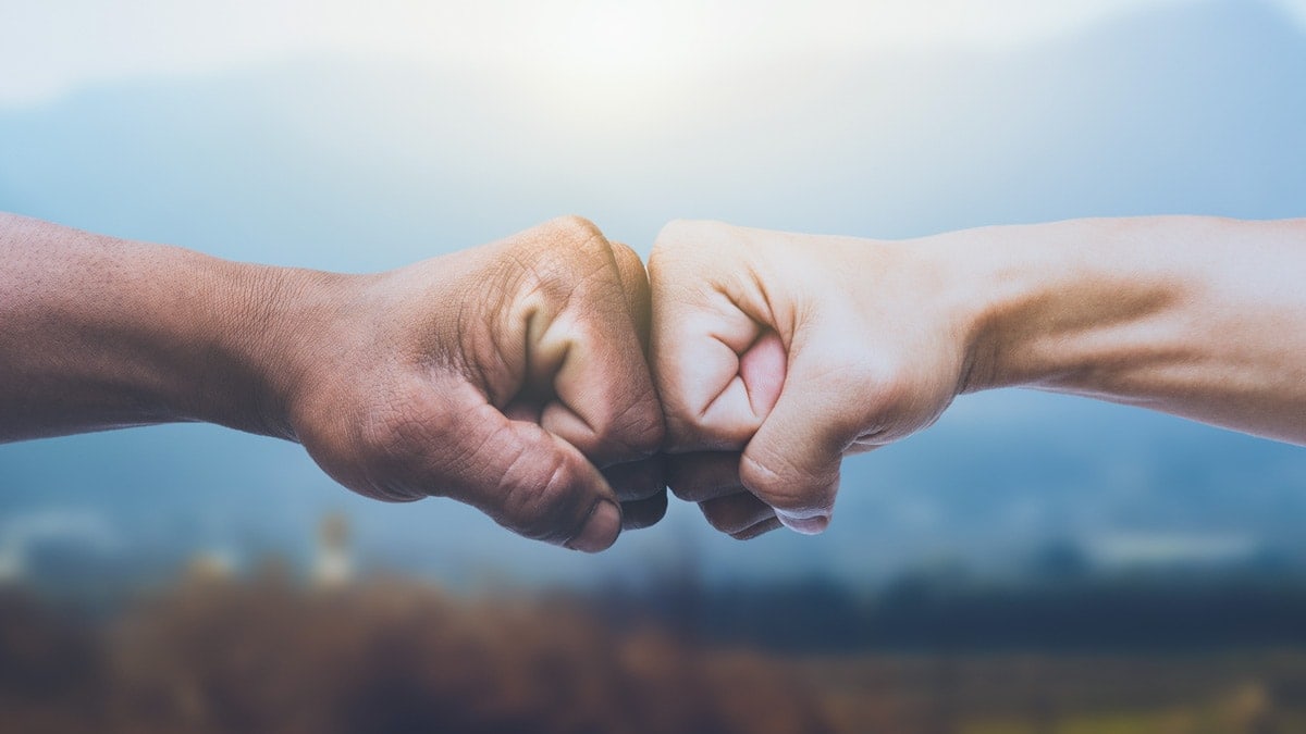 Two fists bumping together in a gesture of unity against a blurred outdoor background.