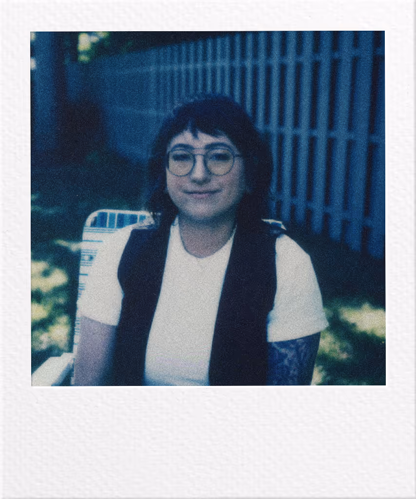 Person with glasses and black vest smiling in front of blue building
