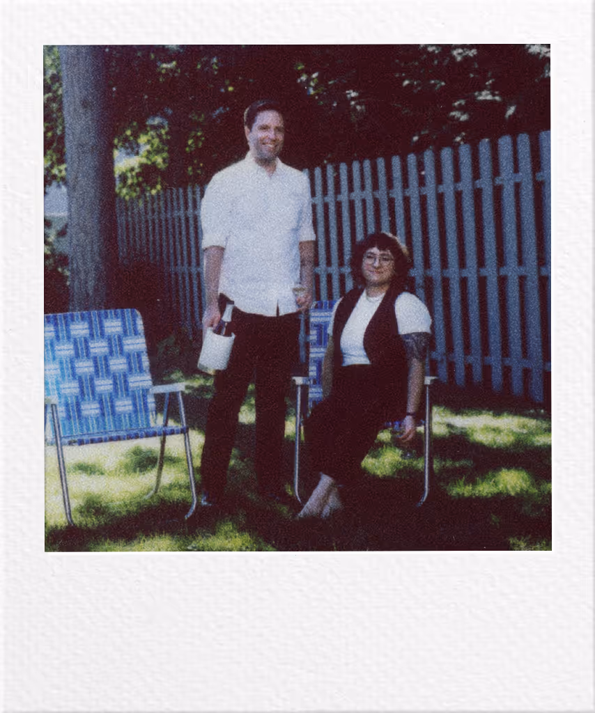 Two people standing in backyard with blue chairs and fence