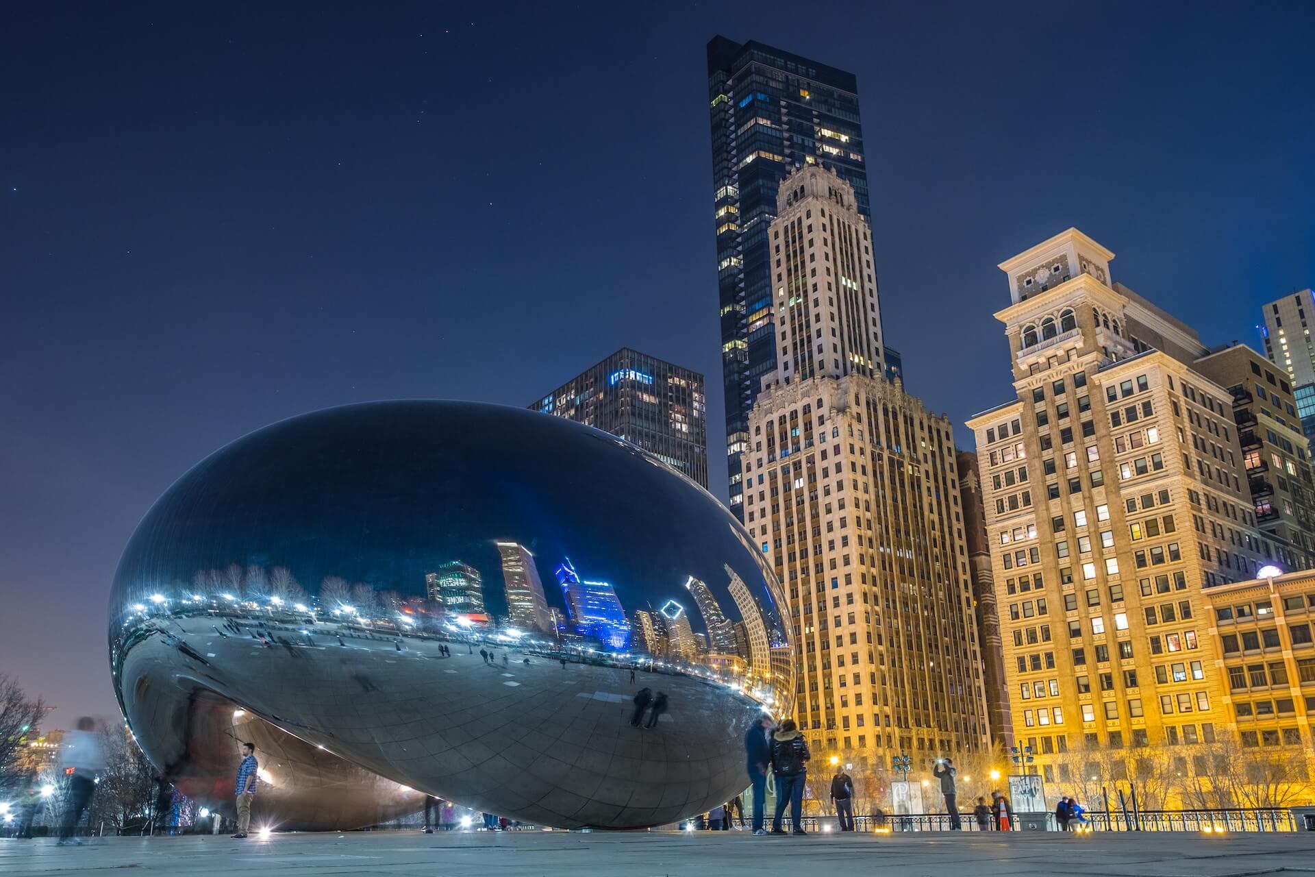 Night view of Chicago's Cloud Gate sculpture with illuminated skyscrapers in the background.