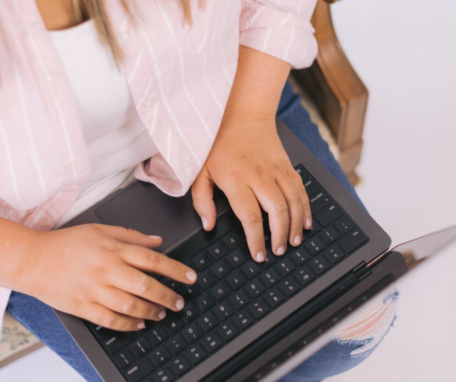 Hands typing on a laptop keyboard while seated with the computer on their lap
