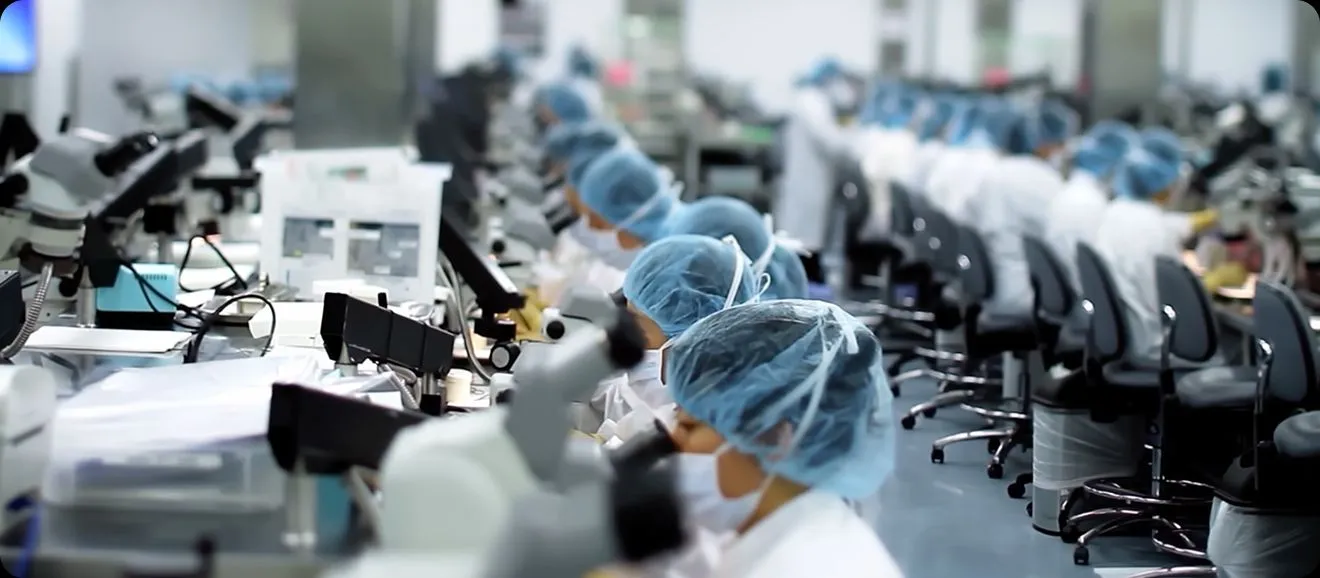 Laboratory with multiple scientists wearing white coats, masks, and blue hair covers working at microscopes.