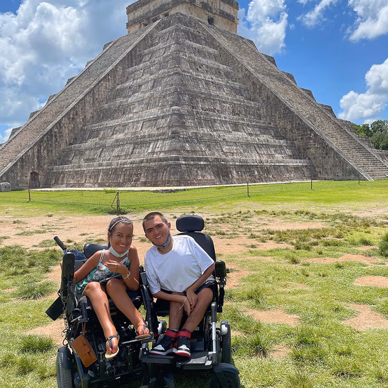 Two people in wheelchairs sitting in front of the Chichen Itza pyramid in Mexico