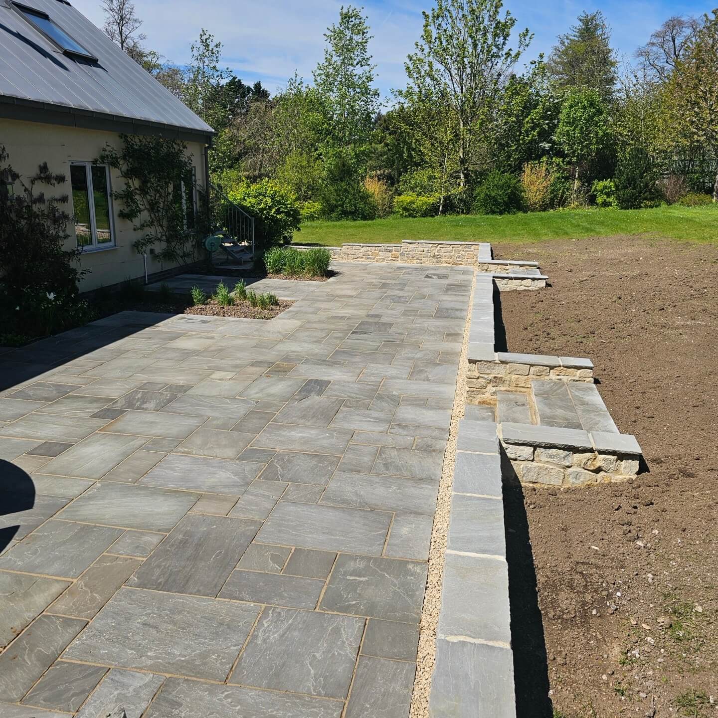 a stone patio with a house and trees in the background