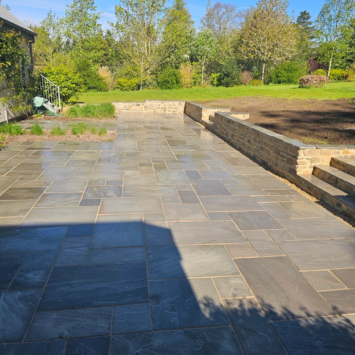 a stone patio with a brick wall and a lawn