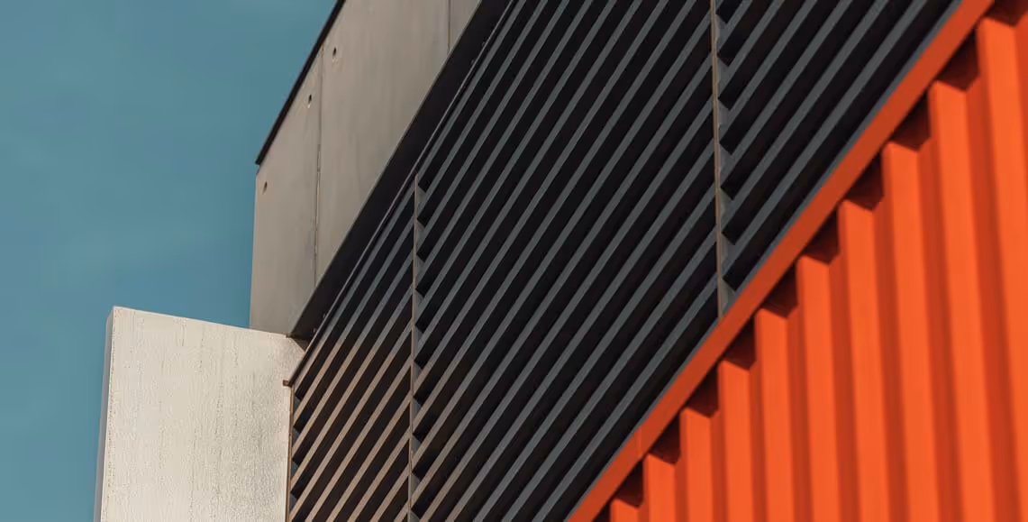 Modern architectural detail of a building with black slats, white panel, and red corrugated wall against a blue sky