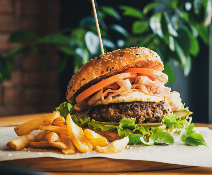 Close-up of a juicy gourmet burger with lettuce, tomato, cheese, onions, and a sesame seed bun, served with crispy fries on the side.