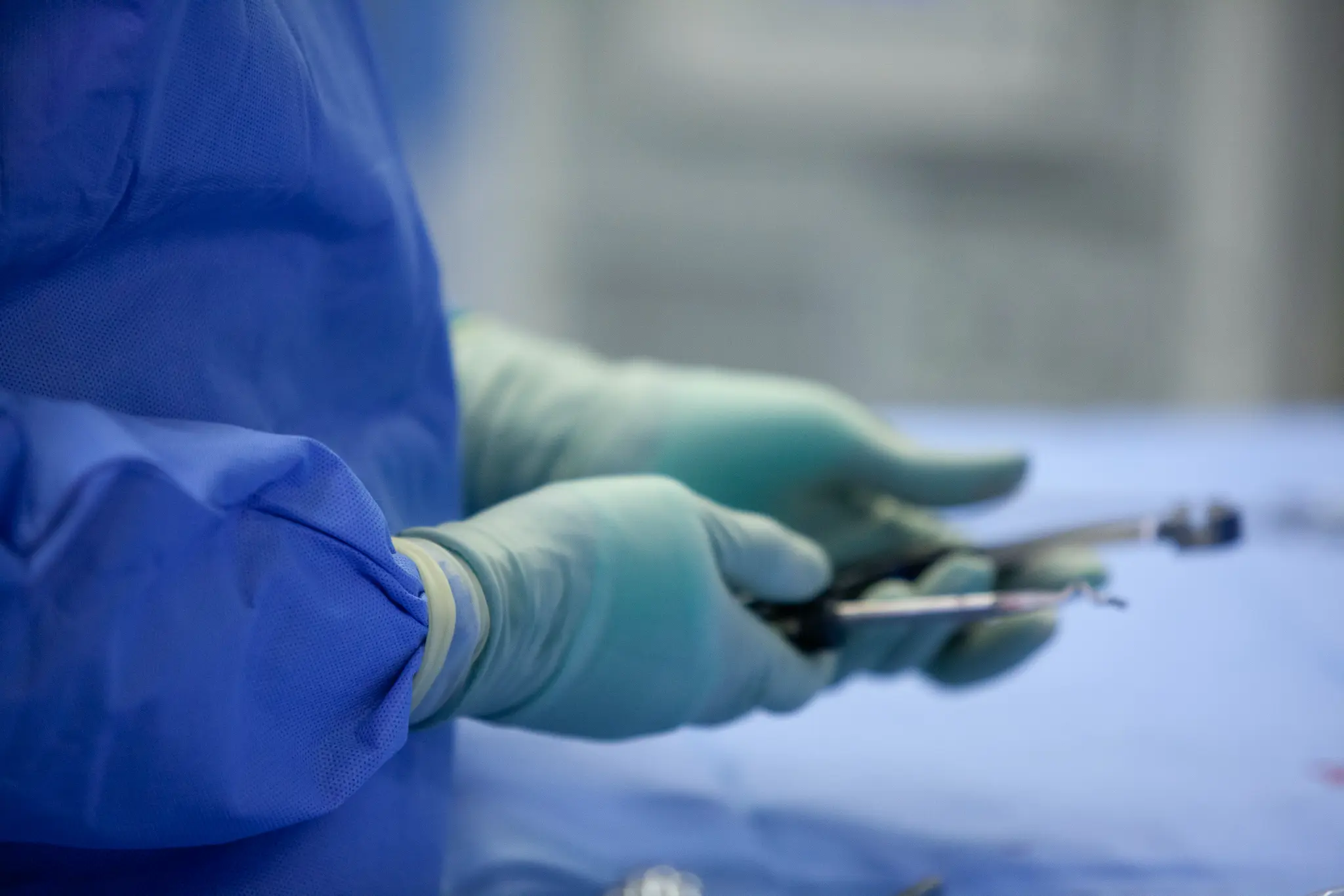 Surgeon wearing blue scrubs and green gloves holding surgical instruments in an operating room.