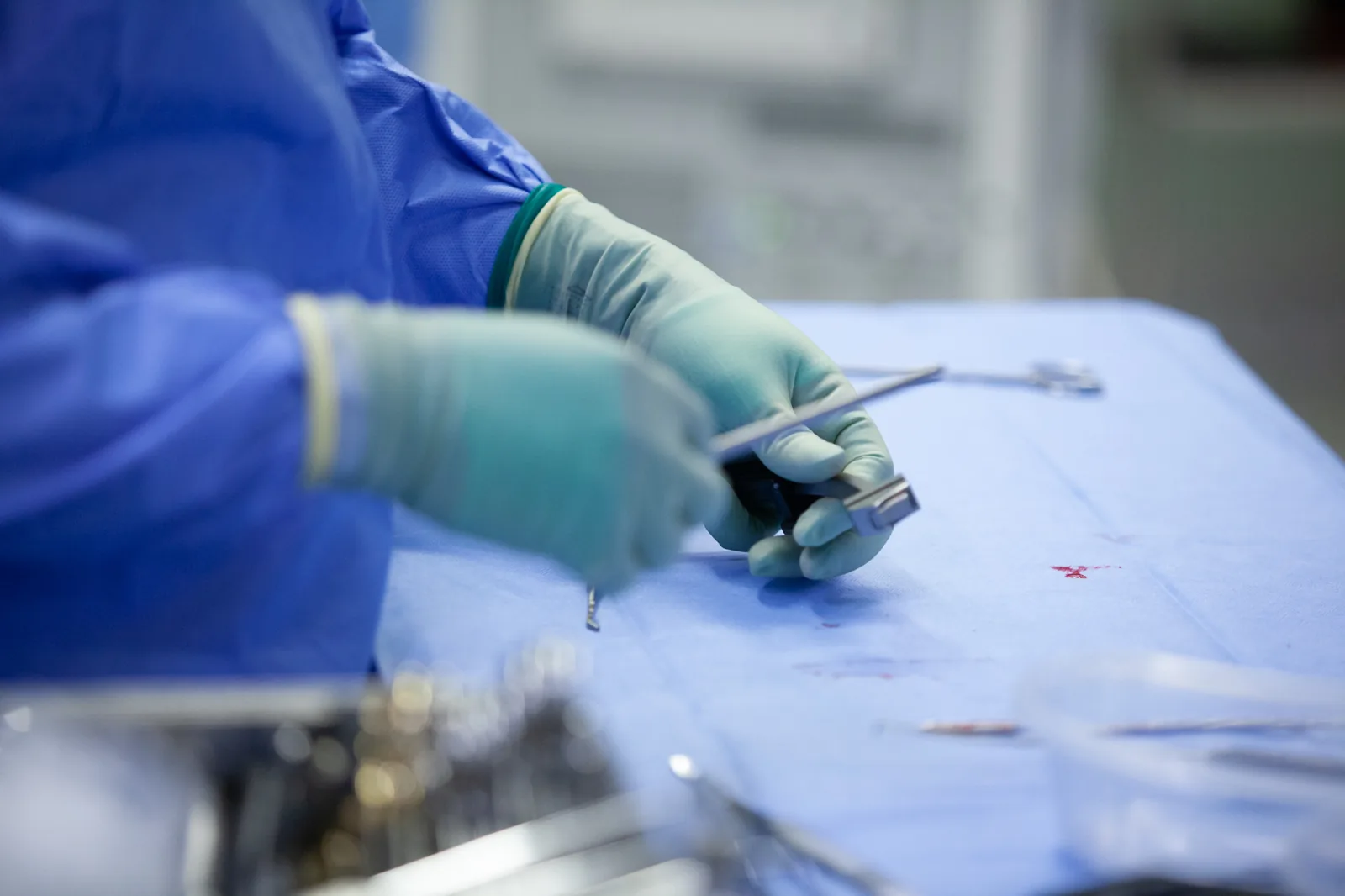 Gloved hands holding a surgical instrument over a sterile drape in an operating theatre