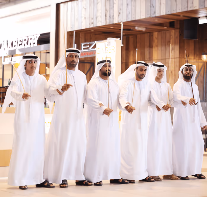 Group of men in traditional Emirati attire performing a cultural dance indoors.
