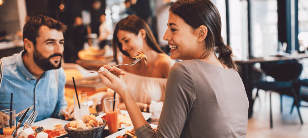 Group of friends enjoying a meal together at a restaurant, smiling and conversing around a table filled with food.