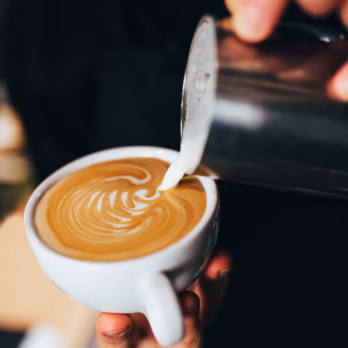 Hand pouring steamed milk into a cappuccino to make latte art