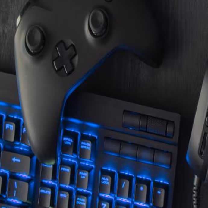 Black gaming controller placed on top of an illuminated blue backlit mechanical keyboard.