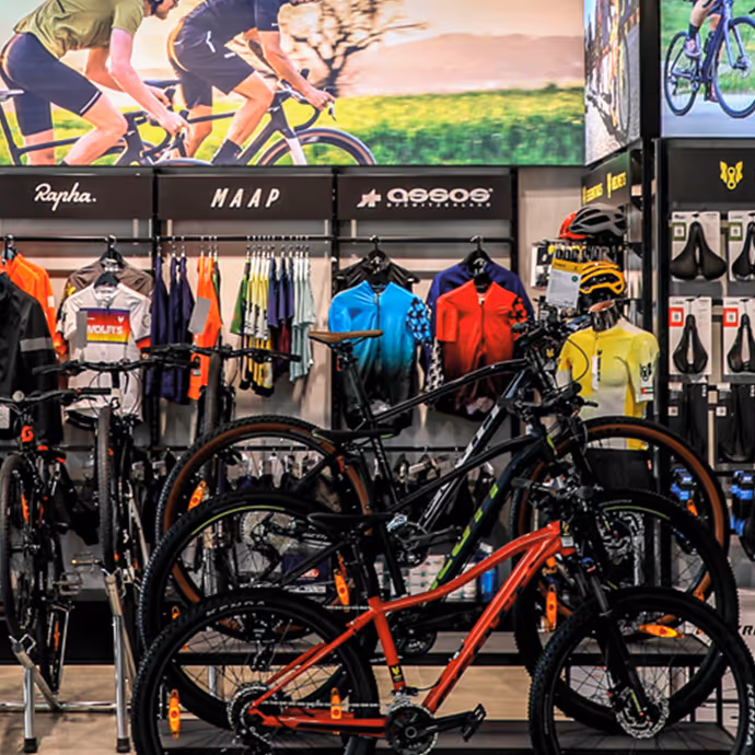 Bicycles and colorful cycling gear on display inside a bike shop with a large poster of cyclists above.