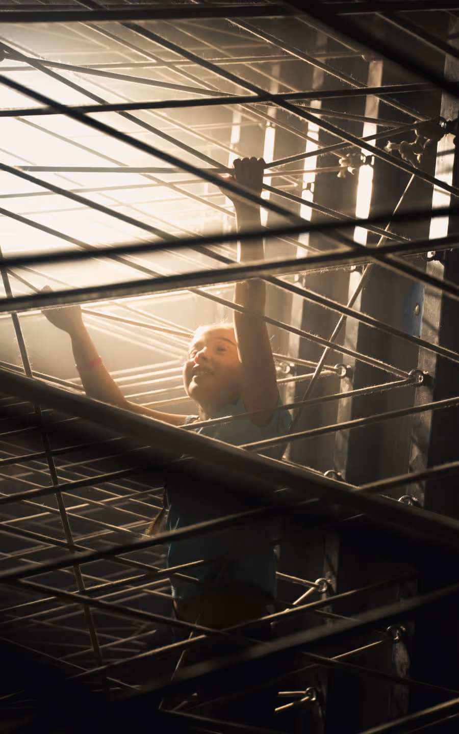 Person climbing through a metal structure with sunlight filtering through the bars.