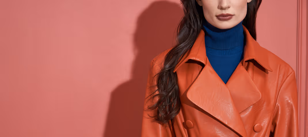 Woman wearing a red leather jacket over a blue turtleneck, standing against a pink wall.