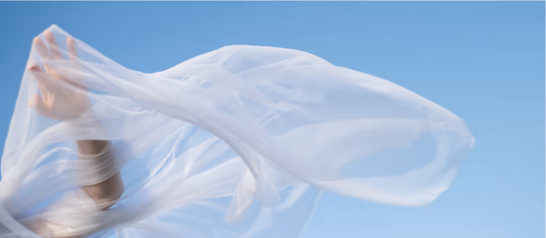Person partially covered by a flowing translucent white fabric against a clear blue sky.