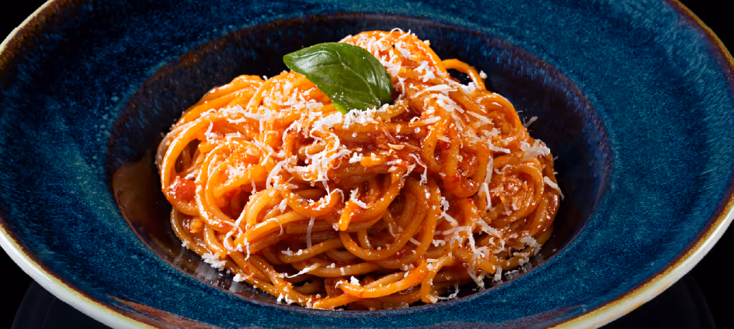 Plate of spaghetti with tomato sauce, grated cheese, and basil garnish served in a deep blue bowl.
