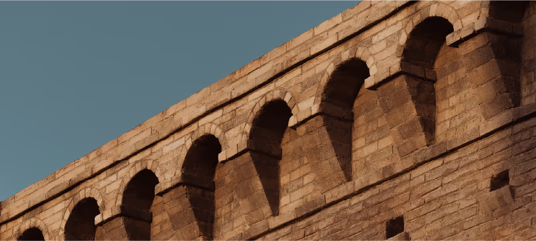 Stone building with a row of arched openings along the top edge under a clear blue sky.
