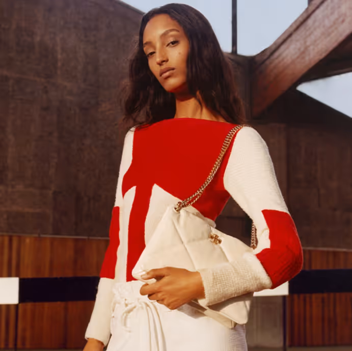 Person posing outdoors wearing a red and white geometric-patterned outfit and holding a beige handbag.