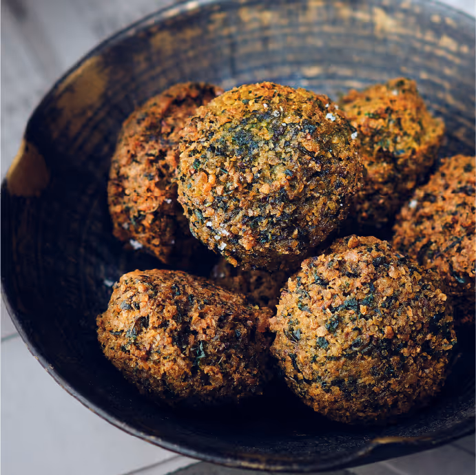 Close-up of a bowl filled with crispy, herb-coated fried balls on a wooden surface.
