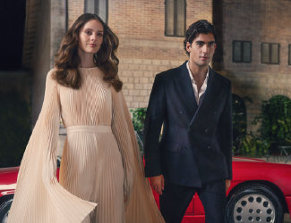 Man and woman in elegant formal attire walking outside a brick building.