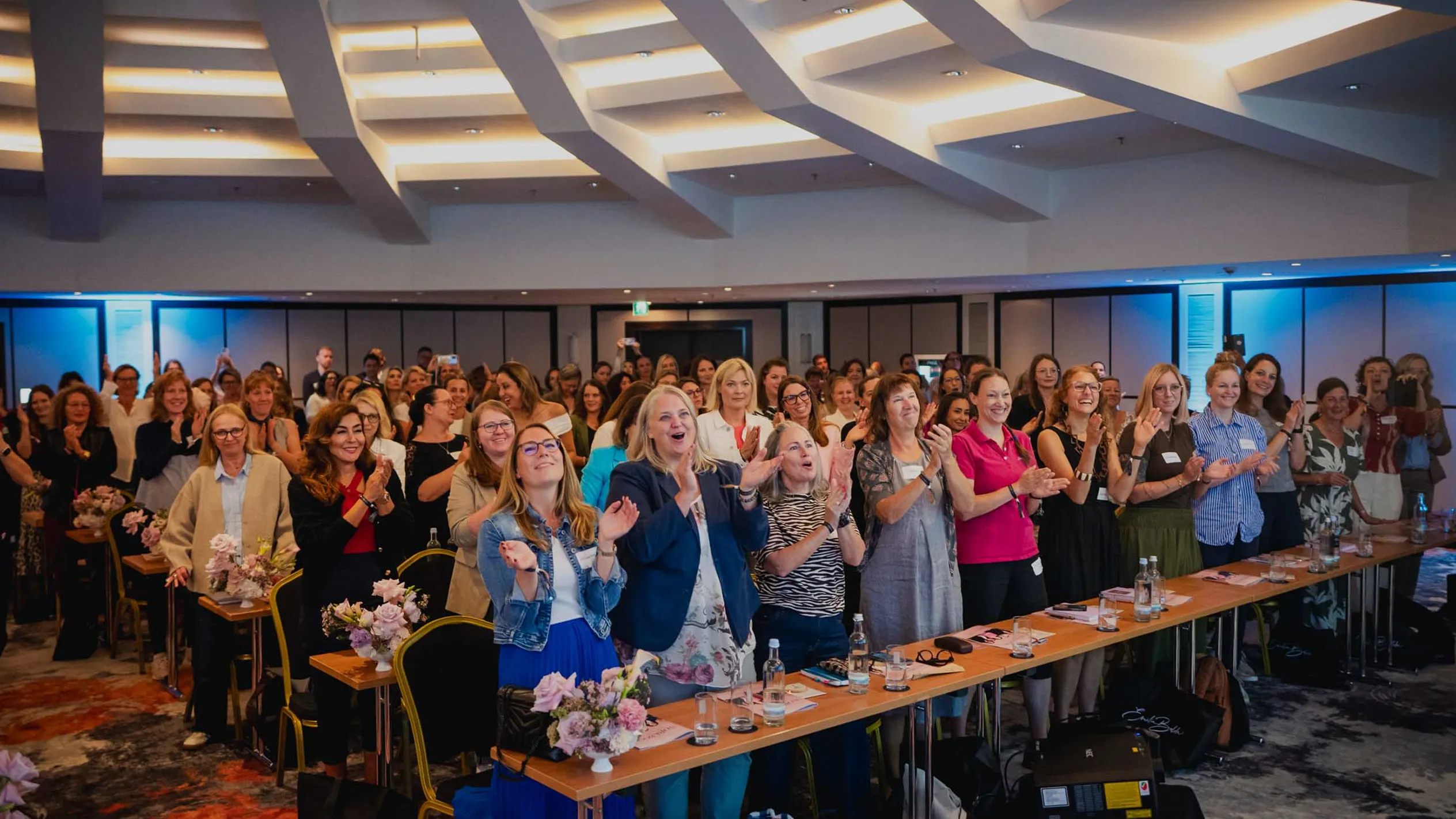 Eine Gruppe junger Frauen, die beim Investiere Dich Frei Summit im Publikum stehen und applaudieren