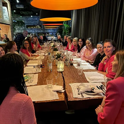 Menschen sitzen an einem langen, mit Kerzen und Gläsern gedeckten Holztisch in einem gemütlichen Restaurant mit orangefarbenen Hängelampen.