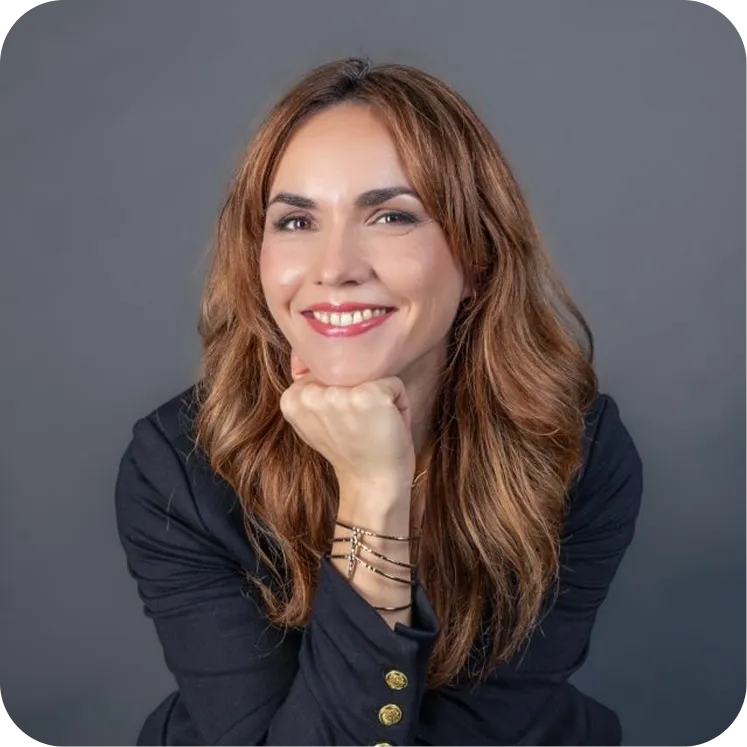 Lächelnde Frau mit roten Haaren, die ihr Kinn auf die Hand stützt, vor grauem Hintergrund.