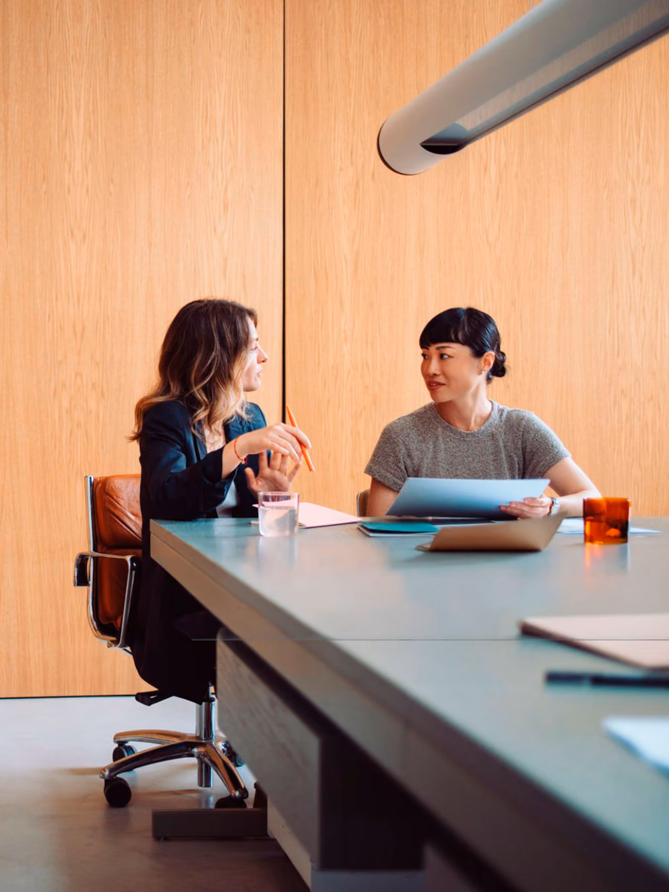 Two women sitting at a conference table having a discussion in a modern office with wooden walls.