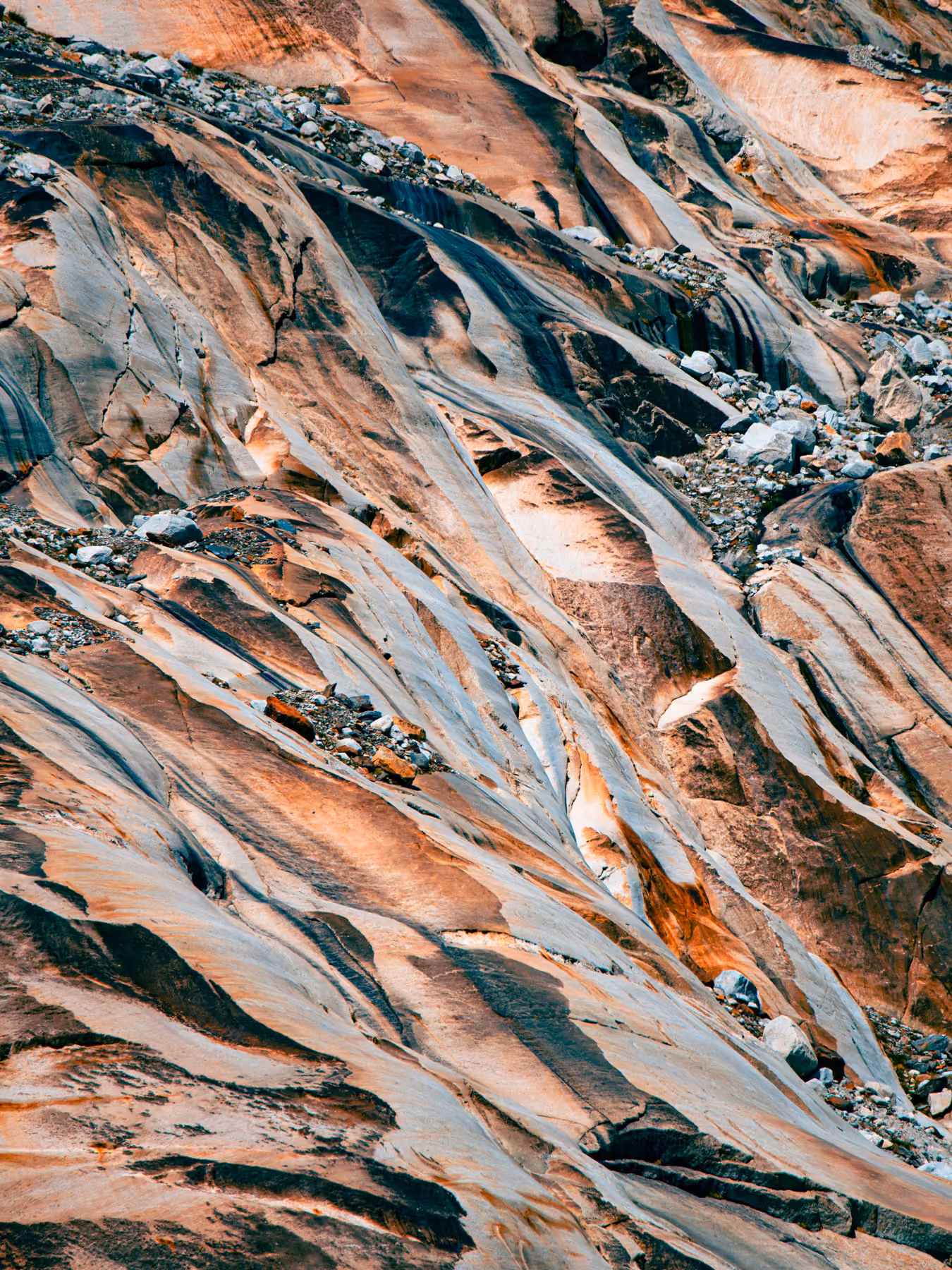 Close-up of rocky, orange and gray textured surface with scattered stones and grooves.