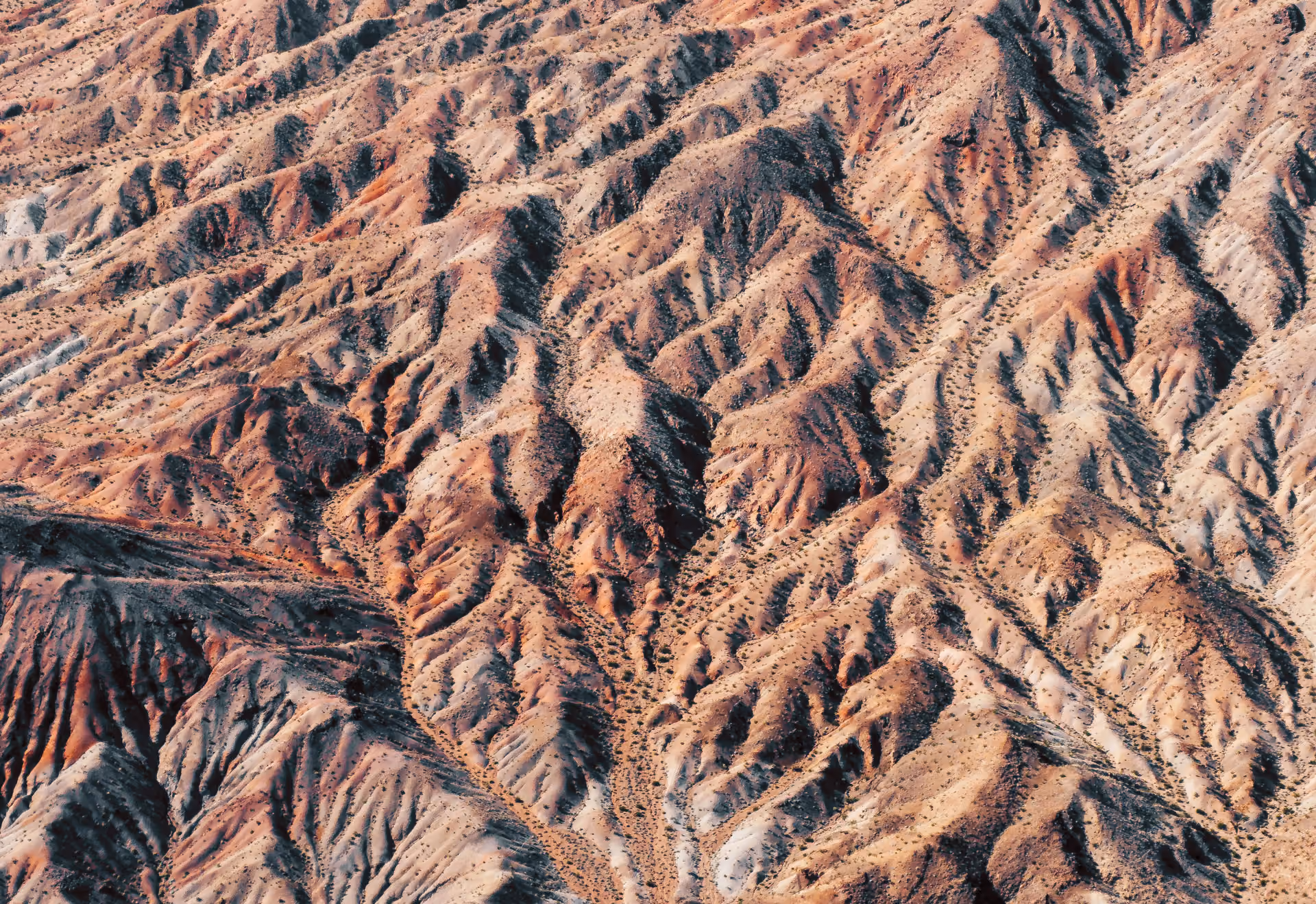 Aerial view of rugged desert terrain with eroded hills and sparse vegetation.