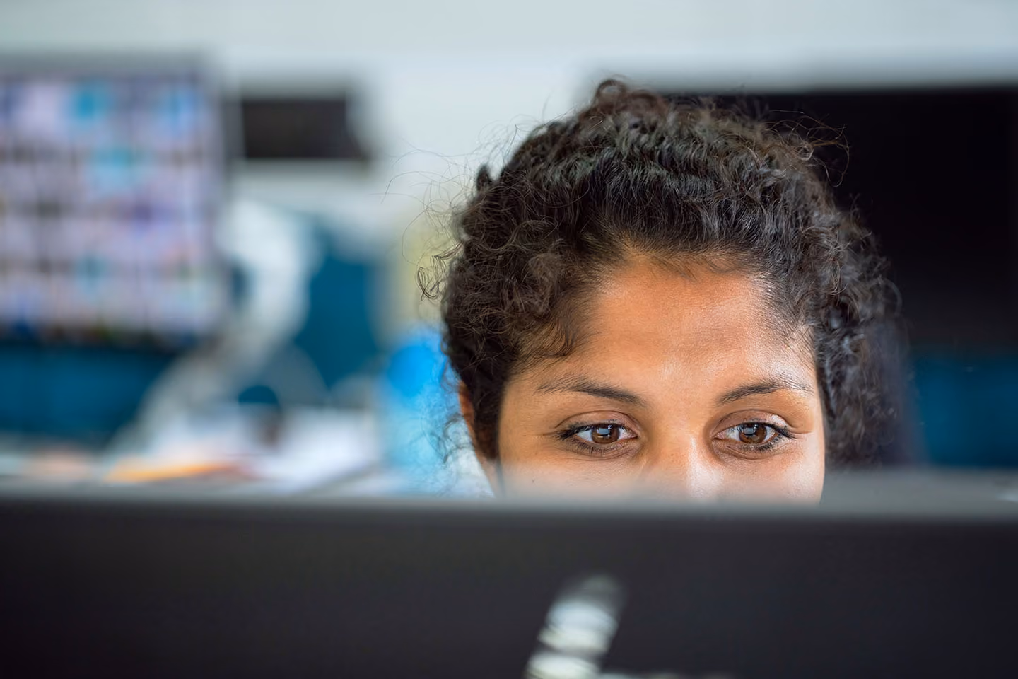 Woman with curly hair focused on her computer screen in an office setting.
