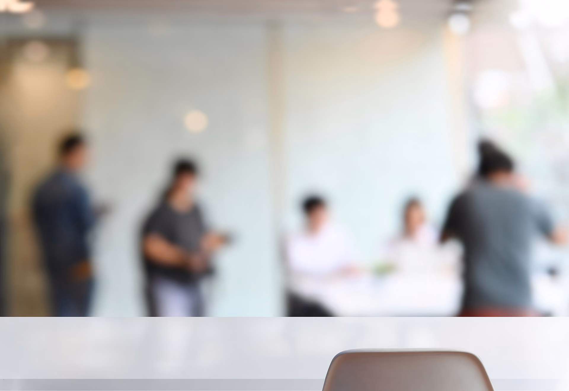 Empty chair in foreground with blurred group of people in a bright office space background.