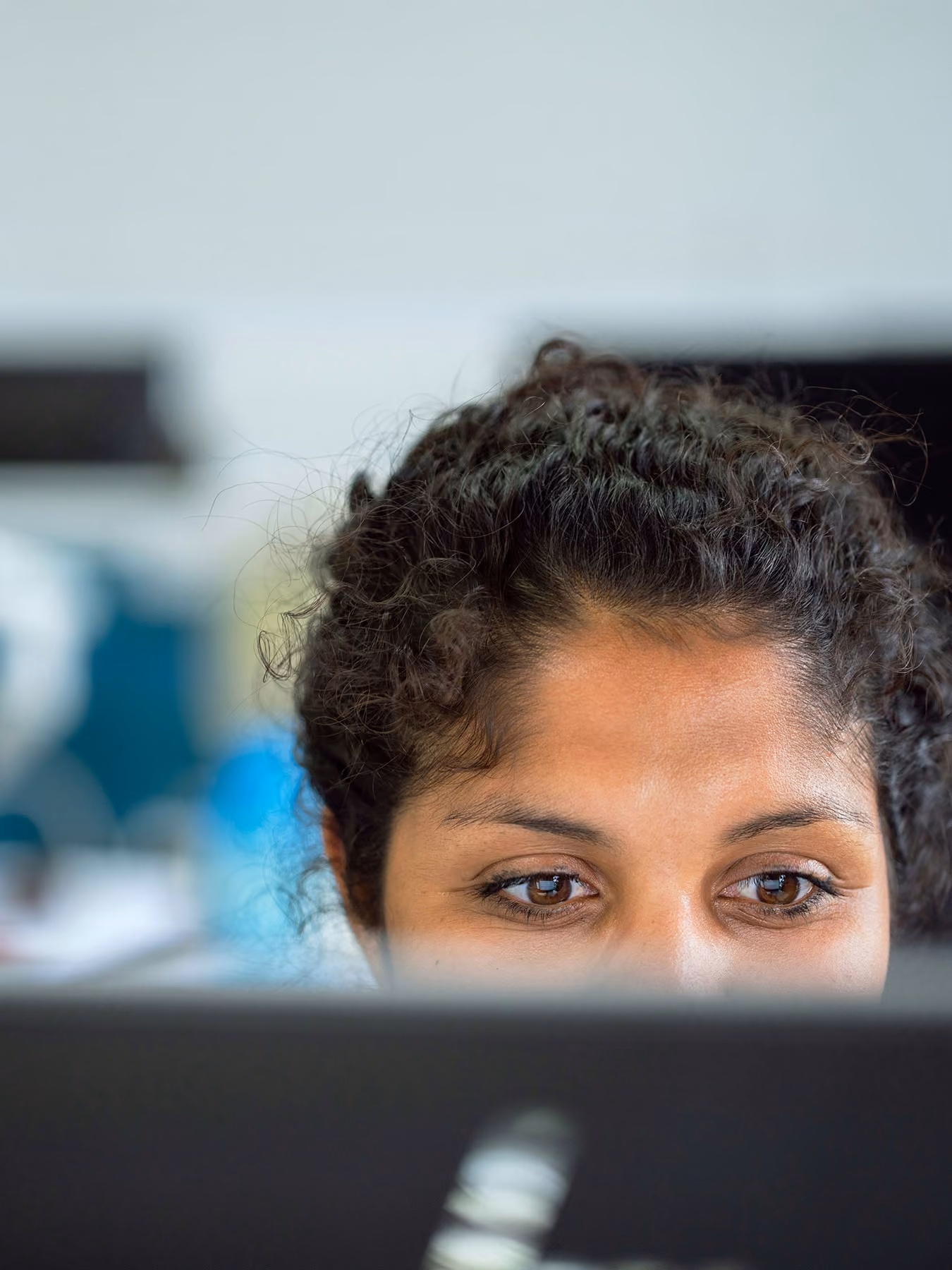 Close-up of a woman with curly hair looking at a computer screen.