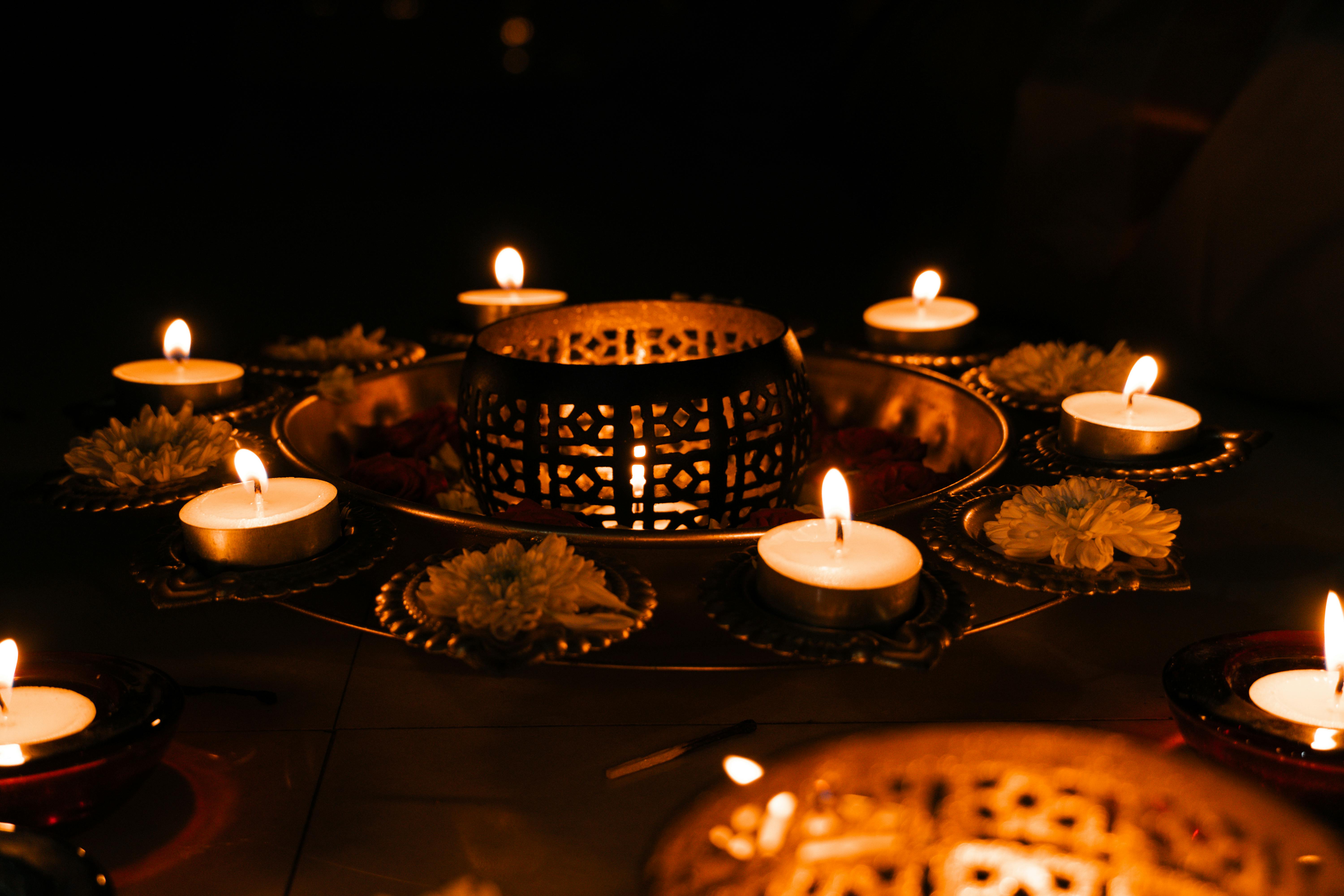 Decorative metal candle holder with lit tea light candles and white flowers arranged in a circle, glowing warmly in the dark.