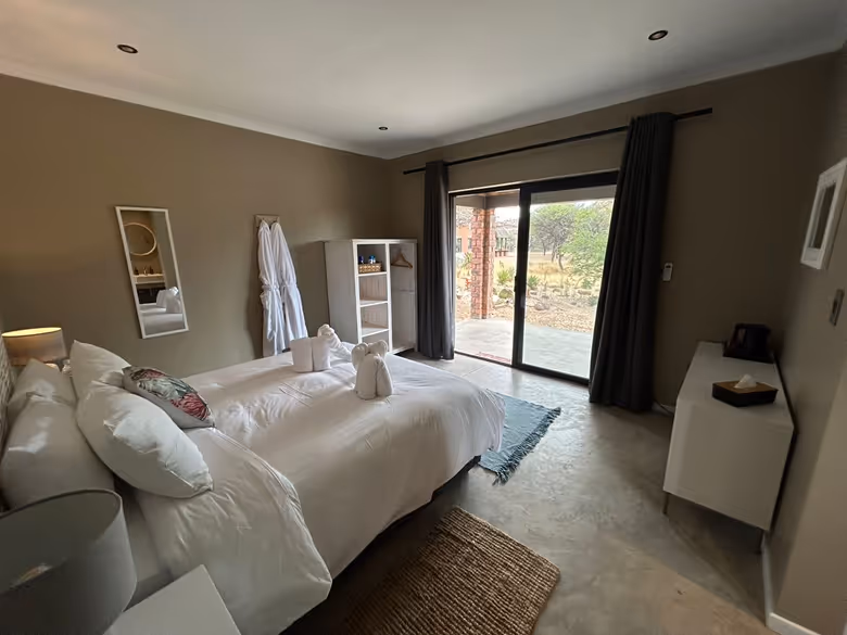 Cozy bedroom with two beds having white linens, towel animals on top, sliding glass door opening to outdoor view, and minimalistic decor.