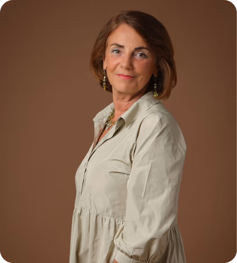 Smiling woman with shoulder-length brown hair wearing light beige dress and earrings against a brown background.