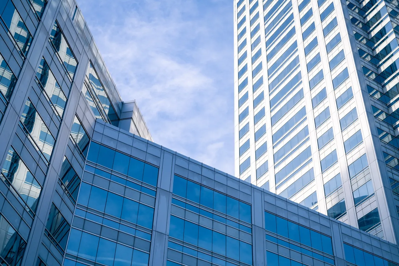 Modern office buildings with reflective blue-tinted glass windows under a partly cloudy sky.
