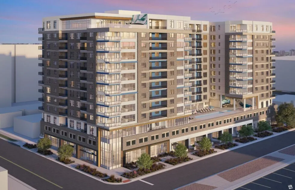 Modern multi-story apartment building with balconies and rooftop lounge area at sunset.