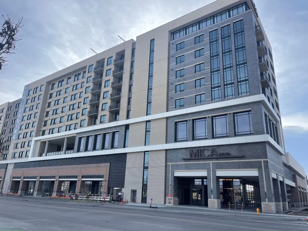 Modern multi-story building with large windows and balconies, labeled 'MICA' and 'NEW LISTING' on the side.