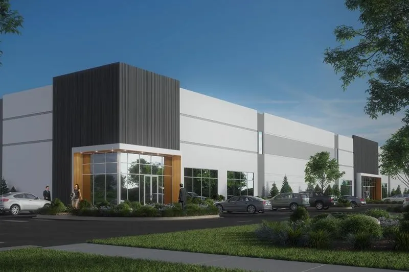 Modern commercial building with large glass entrance and several cars parked outside on a sunny day.