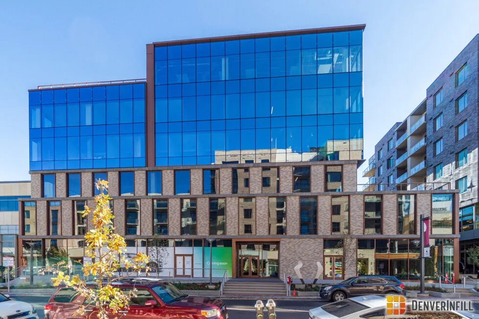 Modern multi-story building with glass and brick facade reflecting surrounding structures under a clear blue sky.