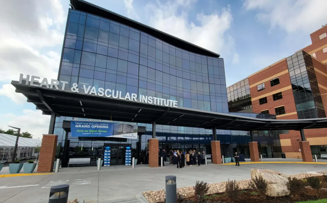 Modern Heart & Vascular Institute building with glass facade and people gathered at the entrance during a grand opening event.