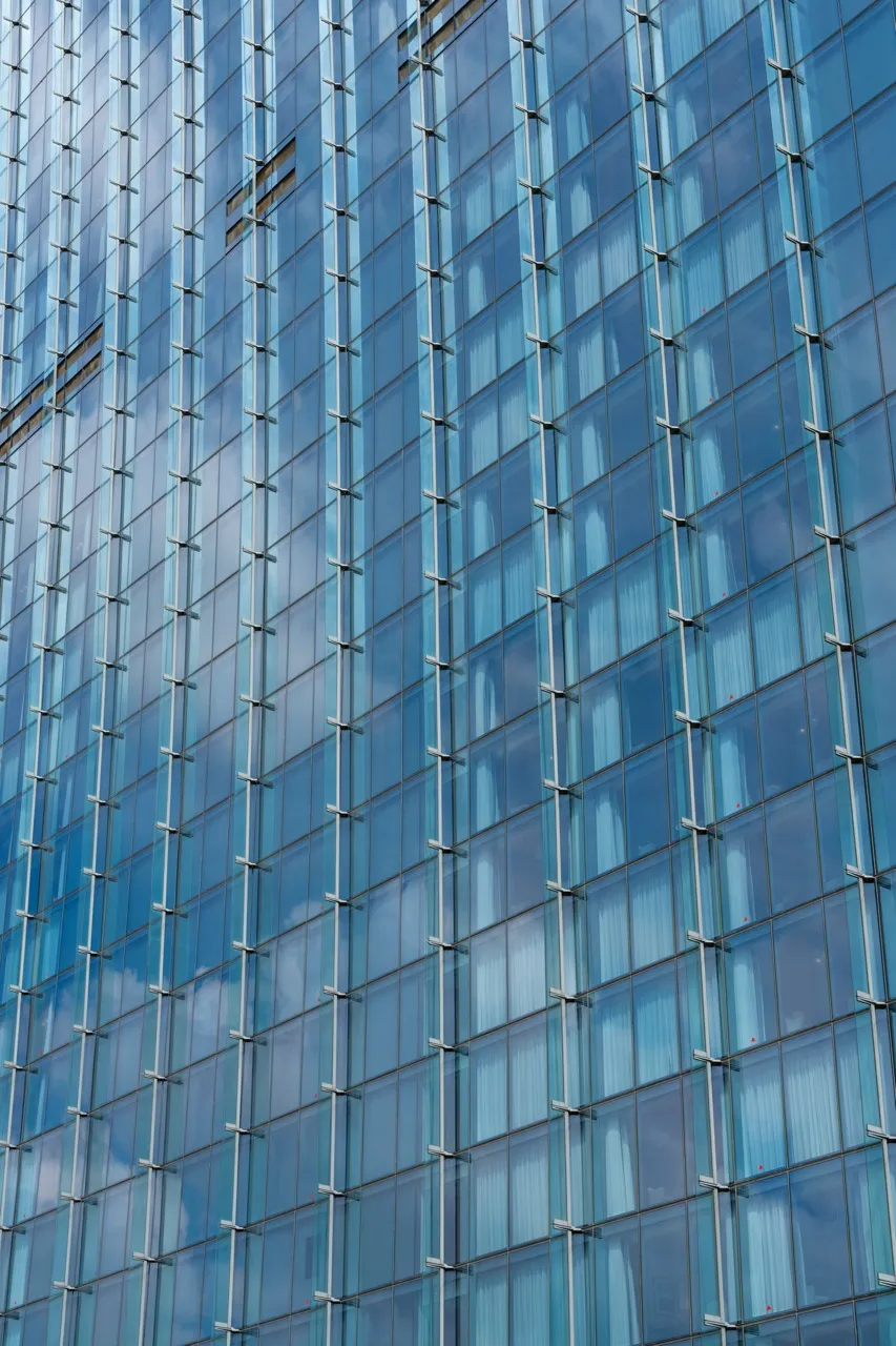 Close-up view of a tall modern building facade with a blue glass curtain wall reflecting clouds.