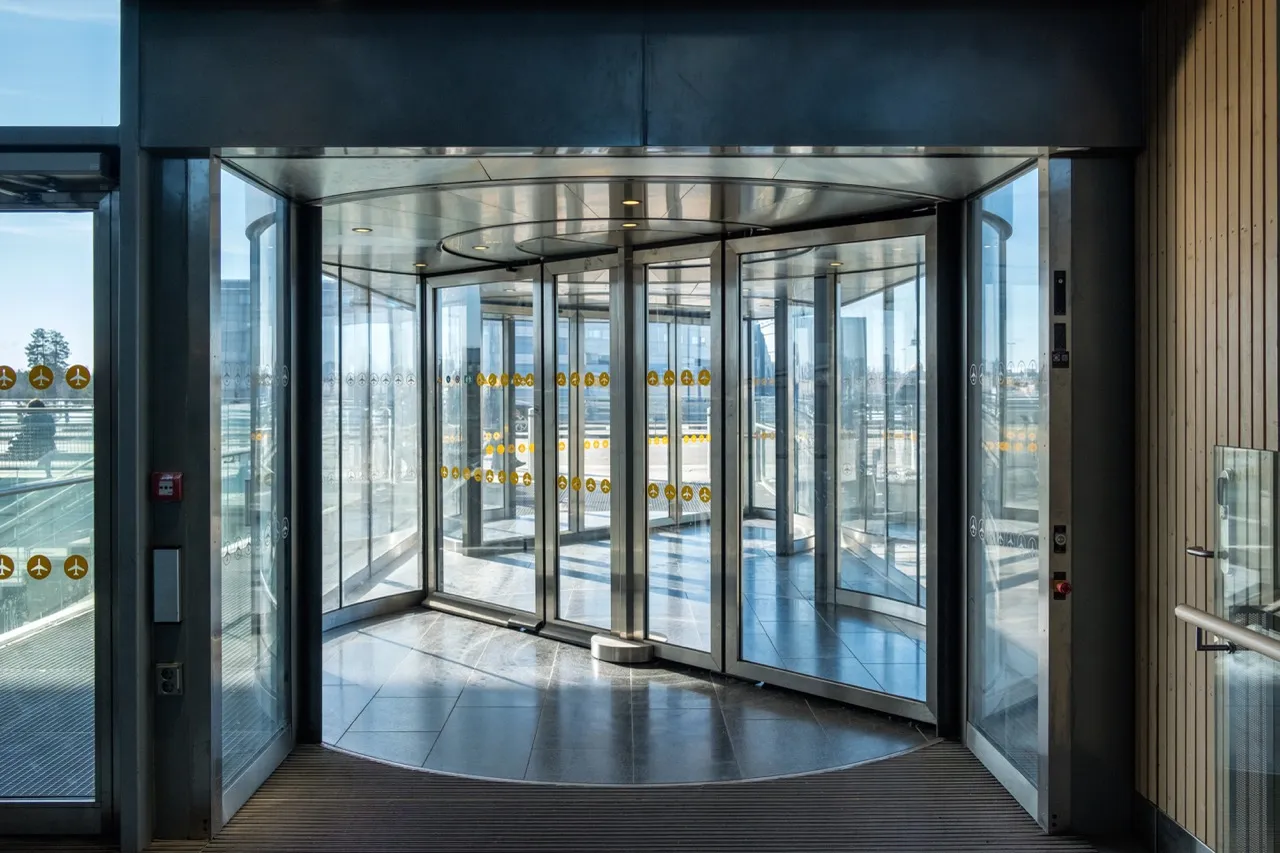 Modern glass revolving door entrance with stainless steel framing and safety decals.