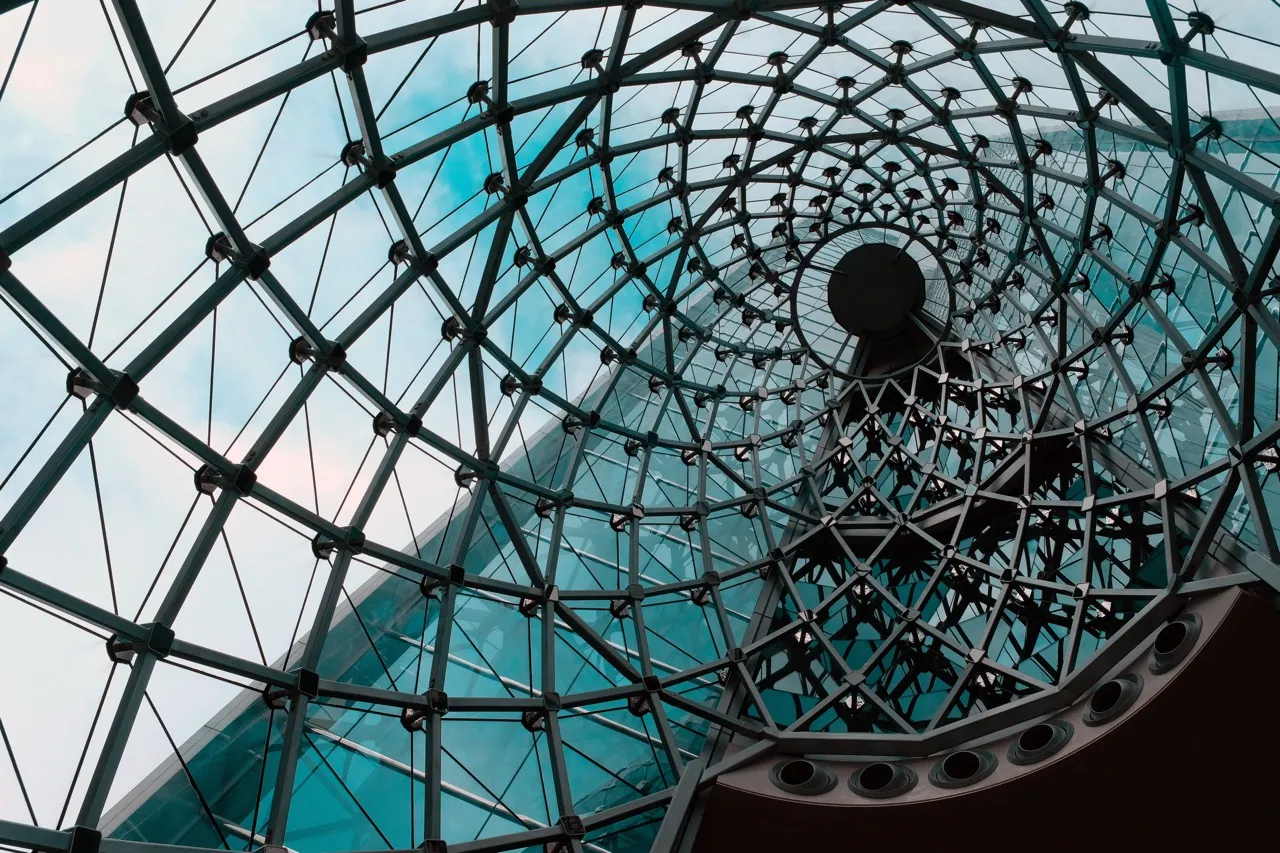 Spiral metal and specialty glass architectural structure viewed from below against a blue sky.