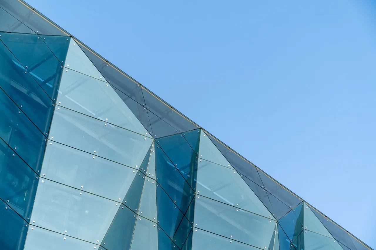 Close-up of a custom glass fabricated building facade with angular panels against a clear blue sky.